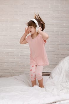 little child girl listening to the music with the headphones and dancing on bed. happy morning