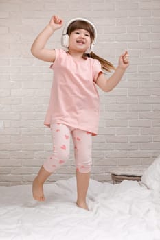 little child girl listening to the music with the headphones and dancing on bed. happy morning
