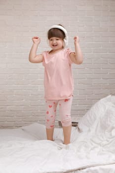little child girl listening to the music with the headphones and dancing on bed. happy morning
