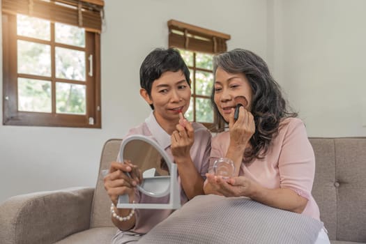 Pretty senior women applying make-up holding small mirrors, happy old friends.