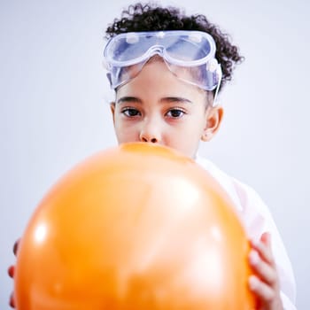 Portrait, science and a kid blowing a balloon in studio on a gray background for a childhood experiment. Children, education and laboratory with a female child wearing goggles while learning.