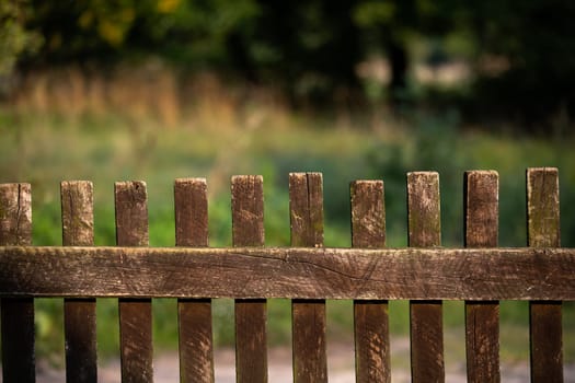 A view of an old wooden fence, handmade from wooden rails. In the background you can see a fuzzy meadow and trees.