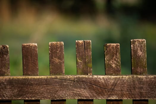 Close frame of wooden old fence built of rails. The background is heavily blurred in shades of green and brown.