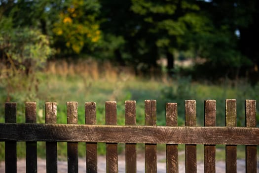 A view of an old wooden fence, handmade from wooden rails. In the background you can see a fuzzy meadow and trees.