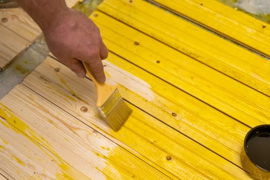 applying the protective composition on the board with a brush. treatment of wood from rotting. the master paints wooden boards.