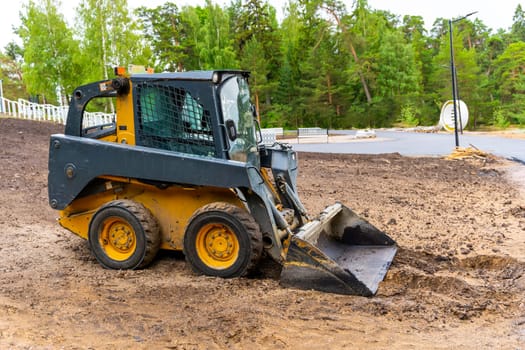 mini loader with bucket. A loader with a bucket clears the site for construction. Land improvement works on the territory. Machine for moving soil, sand and bulk materials