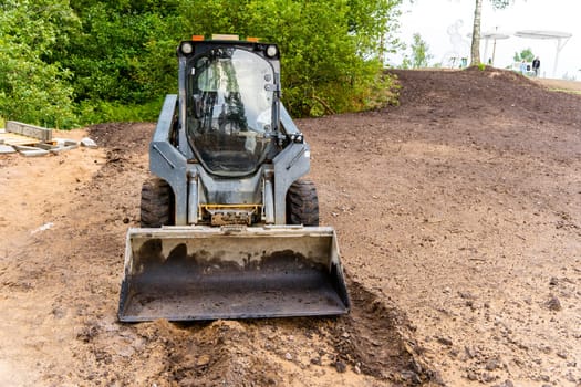 mini loader with bucket. A loader with a bucket clears the site for construction. Land improvement works on the territory. Machine for moving soil, sand and bulk materials