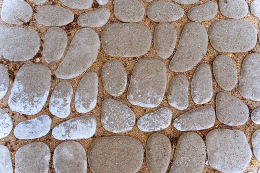 A stone path in a park or city garden. Background of cobblestone pavement. The texture of the stone pavement. A stone-paved road. cobblestone pavement close-up. Sidewalk design. overhead view