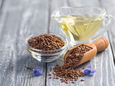 Flax seeds and flax oil. Brown linen seeds, flaxseed oil and blue flax flowers on old gray wooden background. Copy space