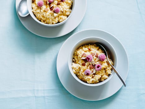Quinoa porrige on tabletop. Two bowl wit quinoa milk porridge with berries and almond. Frozen raspberries in quinoa porrige