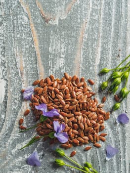 Flax seeds and flax oil. Brown linen seeds, flaxseed oil and blue flax flowers on old gray wooden background. Copy space. Vertical. Top view or flat lay.
