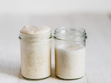 Two glass jars with wheat sourdough starters in different hydration levels. Starter 100 percent hydration - left and starter with higher hydration - right. Copy space