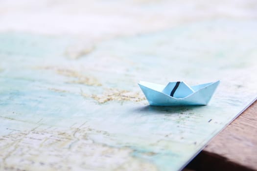 Paper boat on vintage map and wooden background.
