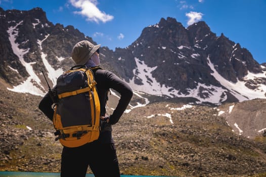 Tourist girl walking with backpacks in the mountains. Hiking concept. Back view of female hiker with backpack relaxing after hike. A woman stands in the mountains and enjoys a picturesque view looking to the side.