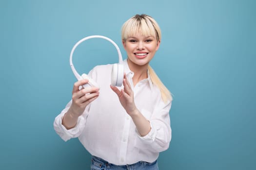 portrait of a stylish young pretty blond secretary woman dressed in a white blouse listening to music through wireless bluetooth headphones. business concept.