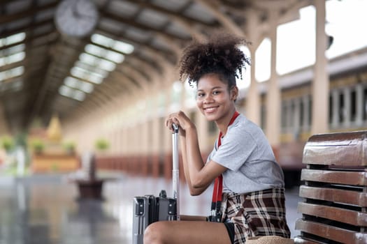 Asian African female tourist traveler holding mobile phone smart phone sitting at train station, Confident smiling teenager girl playing smart phone laptop computer on suit case at station. High quality photo