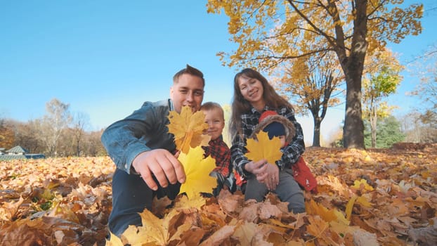A happy family covers the camera lens with a stiff autumn leaf