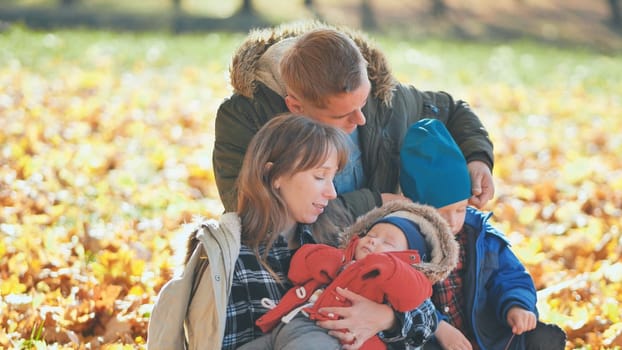 A family and their children enjoy the golden fall in the park sitting on the leaves