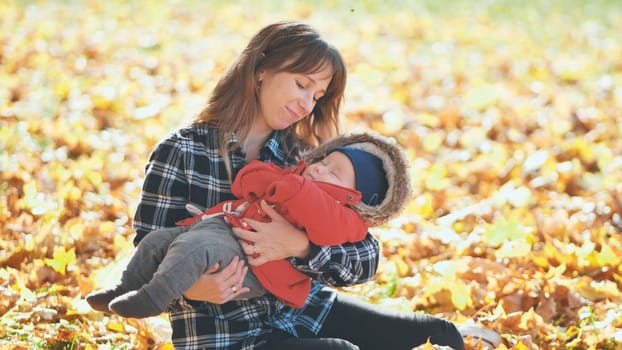 A mother and child in the park in the fall sitting on fallen leaves