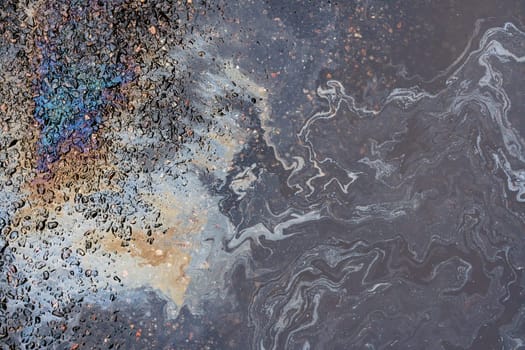Oil stains from leaks in the car engine. Oil after rain makes spots with rainbow reflections refractive sun spectrum. Beautiful color mosaic, abstraction, ecology