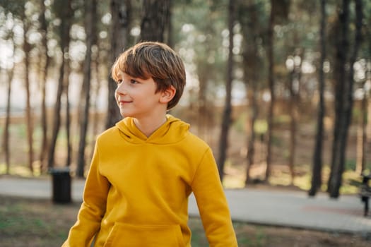 A portrait of a caucasian school boy kid child in a yellow hoodie hiking in the forest city park.