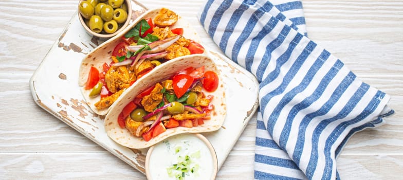 Traditional Greek Dish Gyros: Pita bread Wraps with vegetables, meat, herbs, olives on rustic wooden cutting board with Tzatziki sauce, olive oil top view, white wooden summer background.