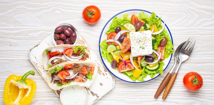 Traditional Greek Food: Greek Salad, Gyros with meat and vegetables, Tzatziki sauce, Olives on White rustic wooden table background top view. Cuisine of Greece