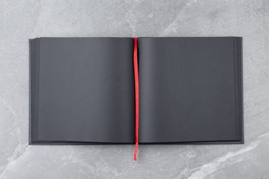 Open black notebook with blank pages and red bookmark on gray marble background. Top view.