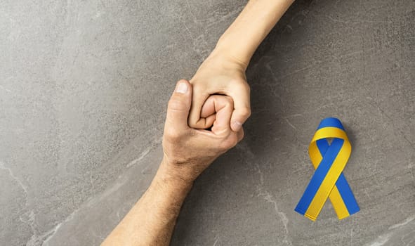 hand holding tight hand of child with yellow and blue ribbon on marble. concept needs help and support, truth will win