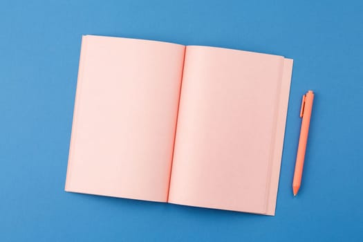 Pink notebook with pen on blue isolated background. Flat lay. Top view.