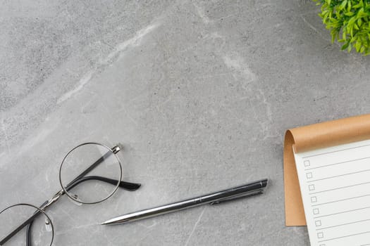 Open notepad, pen, glasses and potted plant on gray marble background. Top view. Office desk concept.