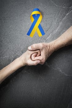hand holding tight hand of child with yellow and blue ribbon on marble. concept needs help and support, truth will win