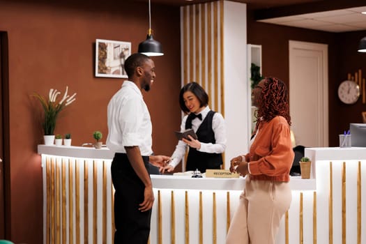 Hotel worker registering guests in lobby, checking booking information and doing check in before showing room. Receptionist at front desk working with registration forms for accommodation.