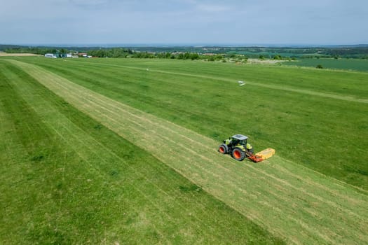 With aid of rotary cutting device, tractor is mowing field. Top view of mowing grass on field.