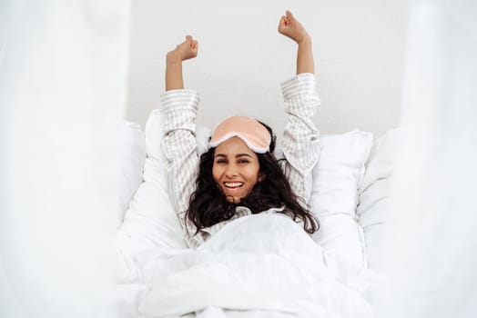A young woman of Arab appearance and woke up in her bed and stretched. Girl is satisfied with a healthy sleep and is ready to start this day with a smile of joy. Woman in a cozy snow-white setting