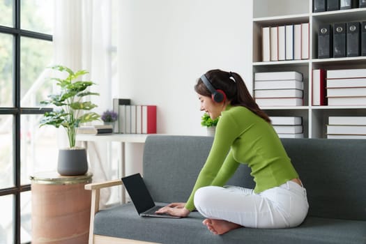 Young asian relaxed smiling pretty woman relaxing with laptop at home. Female feeling joy enjoying with mobile phone on cozy couch.