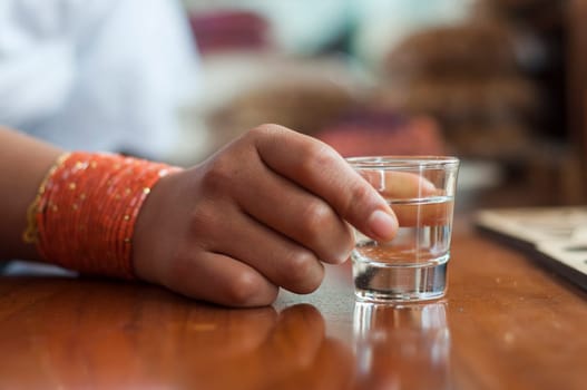 closeup of an indian girl hand holding a shot of alcohol on a wooden table. High quality photo