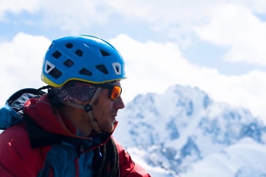A man in special mountaineering glasses with a mirror-effect orange color, takes care of his eyesight and safety in the snowy mountains. The hiker travels in the mountains, is engaged in climbing.
