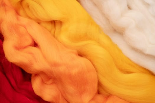 White, yellow, beige and red merino wool for felting as background texture.