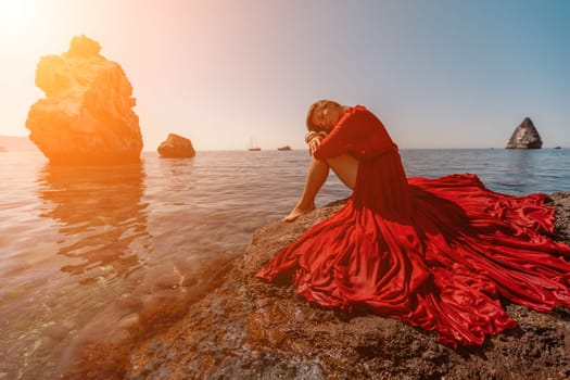 woman sea red dress. Beautiful sensual woman in a flying red dress and long hair, sitting on a rock above the beautiful sea in a large bay