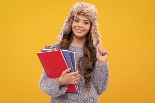 express positive emotion. winter fashion. smiling kid with curly hair in hat. back to school. teen girl in knitwear on yellow background. portrait of child wearing warm clothes holding workbook.