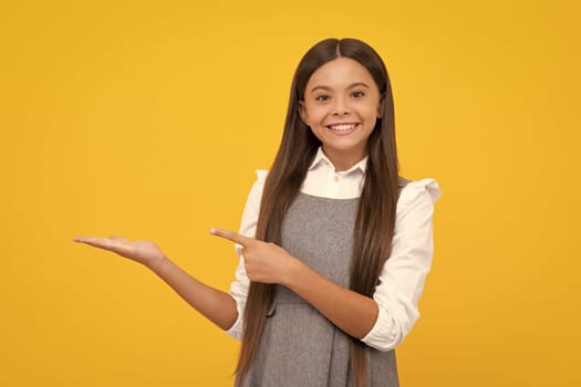 Happy girl face. Close up portrait of teenager child girl showing at copy space, pointing to ads advertising, isolated over yellow background. Mock up copy space