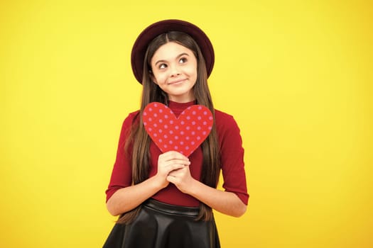 Happy teenager portrait. Cheerful lovely romantic teen girl hold red heart symbol of love for valentines day isolated on yellow background. Smiling girl