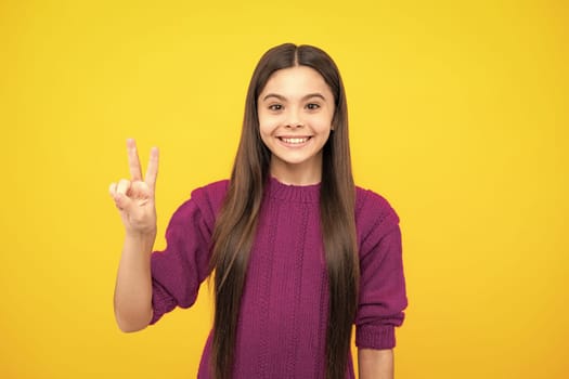 Portrait of funny cheerful teenager child girl showing v-sign isolated over yellow background