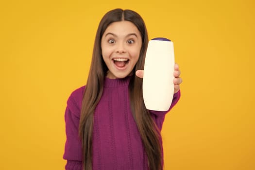 Excited face. Teenager child girl showing bottle shampoo conditioners or shower gel isolated on yellow background. Hair cosmetic product. Mock up bottle. Amazed expression, cheerful and glad