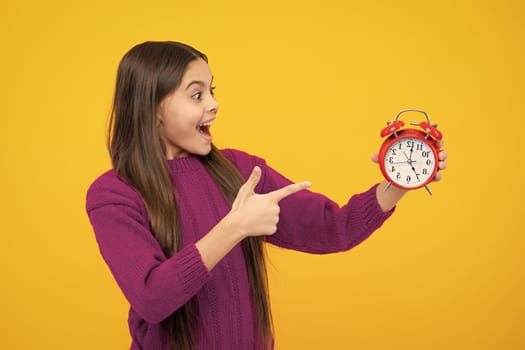Excited face. Portrait of teenage girl with clock alrm, time and deadline. Studio shot isolated on yellow background. Amazed expression, cheerful and glad