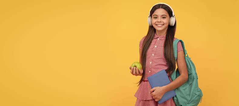 smiling school child in headphones carry backpack and workbook with apple for lunch. Portrait of schoolgirl student, studio banner header. School child face, copyspace