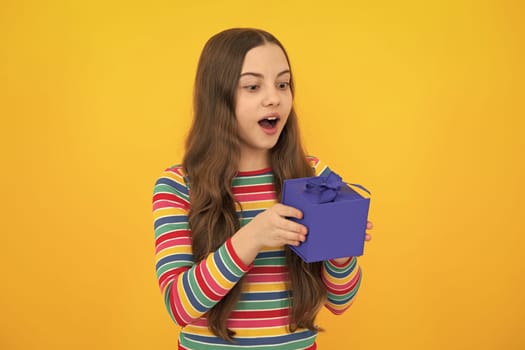 Child with gift present box on isolated studio background. Gifting for kids birthday. Amazed surprised emotions of young teenager girl