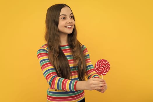 Cool teen child with lollipop over yellow isolated background. Sweet childhood life. Teen girl with yummy lollipop candy