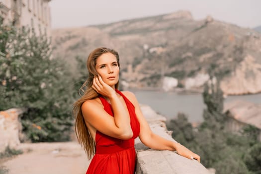 Woman red dress. Summer lifestyle of a happy woman posing near a fence with balusters over the sea